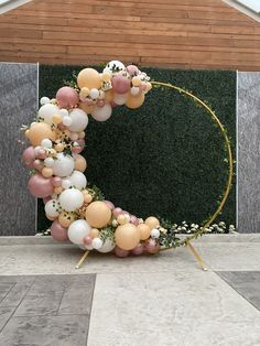 a wreath made out of balloons and greenery on the ground in front of a building