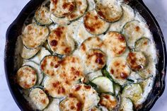 a skillet filled with cheese and zucchini on top of a white counter