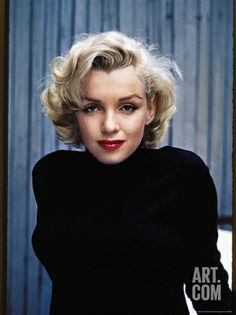 a woman with blonde hair sitting on a chair in front of a wooden wall and wearing a black sweater