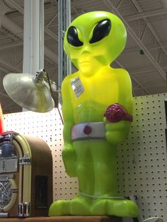 a green alien statue sitting on top of a shelf next to a clock and other items