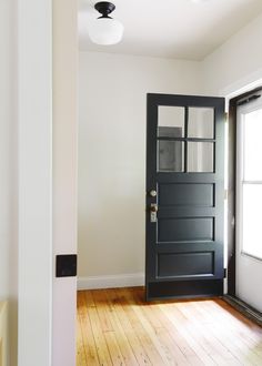 an empty room with a black door and wood flooring is seen in this image