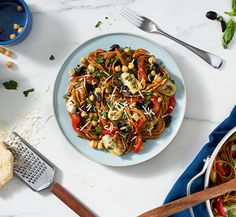 a white plate topped with pasta and veggies next to a bowl of salad