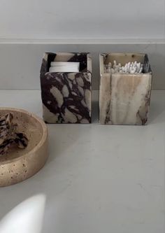 three marble boxes sitting on top of a counter next to a bowl and container with toothbrushes in it