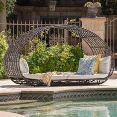 an outdoor wicker day bed with pillows on it next to a pool and fence