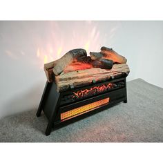 an open fire pit with logs and flames on the top, in front of a white wall