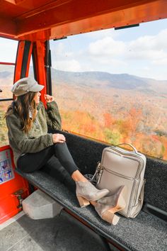 a woman sitting in the back of a bus looking out at mountains and trees with her purse