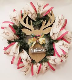 a wooden sign that says welcome hanging on a wall next to a wreath with deer antlers