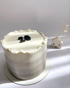 a cake with white frosting and two black decorations on top, sitting next to a dice