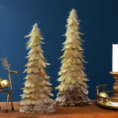 three small christmas trees sitting on top of a wooden table next to a candle holder