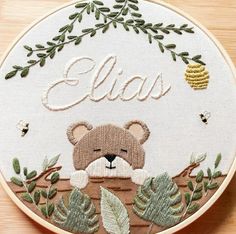 a close up of a embroidery on a wooden surface with leaves and a teddy bear