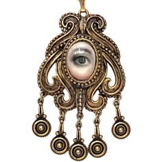 A Lover's Eye original oil painting on a vintage pendant with dangling details measuring 1.75" by 2.75"and a 12" double chain. THE HISTORY: Lover's Eyes were a jewelry trend c.1785-1830 of brooches set with tiny watercolor portraits on ivory. Since they were cropped to eyes, they were in many ways more direct and intimate than traditional miniature portraits; but also because they were just eyes, they were often used as daring public testimonies of clandestine love affairs with mystery lovers. T Antique Brass Dangle Jewelry, Victorian Style Round Pendant Jewelry, Antique Teardrop Jewelry In Antique Gold, Antique Gold Pendant Necklace With Charms, Antique Gold Jewelry With Large Pendant As Gift, Antique Pendant Jewelry With Vintage Charm, Antique Gold Pendant Jewelry With Charms, Gold Dangle Jewelry With Antique Finish, Handmade Victorian Jewelry