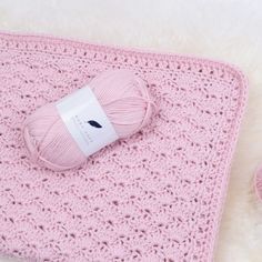 a pink crocheted blanket and two balls of yarn