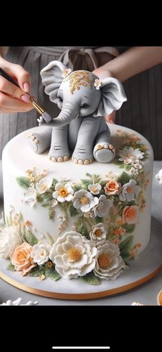 a woman is decorating a cake with an elephant figurine and flowers on it