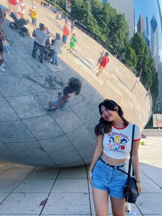 a woman standing in front of a large mirror ball with people walking around it on the other side