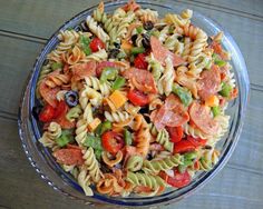 a pasta salad with pepperoni, olives, tomatoes and green peppers in a glass bowl