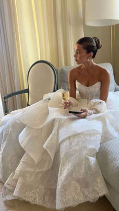 a woman in a wedding dress sitting on a bed with a glass of wine and a book