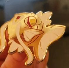 a hand holding a gold colored pokemon brooch