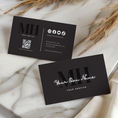 two black business cards sitting on top of a white marble table next to dried grass