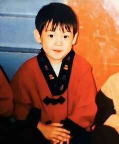 a young boy sitting on the ground wearing a red robe