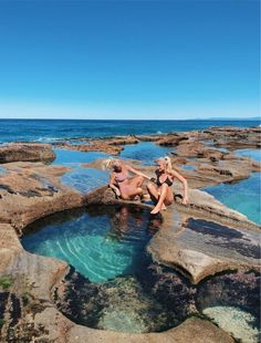 two women in bikinis sitting on rocks by the ocean