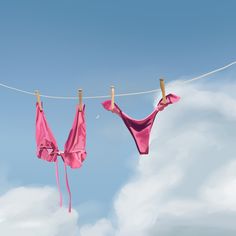 two pink cloths hanging on a clothesline with blue sky and clouds in the background