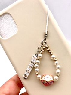 a hand holding a cell phone case with a charm attached to the back of it