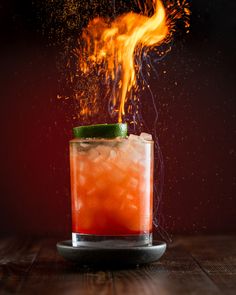 a drink with orange and green garnish on the rim sitting on a wooden table