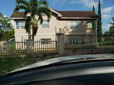 a car is parked in front of a house with a gate and palm trees behind it