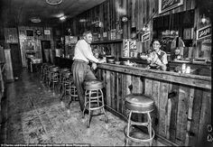 black and white photograph of two men sitting at the bar in a restaurant with stools