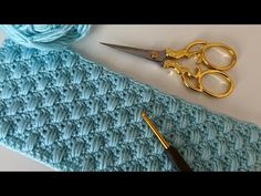 a pair of gold scissors sitting on top of a blue knitted scarf next to a crochet flower