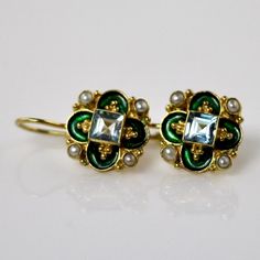 This unique Arts & Crafts Movement design showcases an onyx, iolite, blue topaz, emerald, or garnet set in a cloverleaf of emerald-green or royal blue enamel work, accented with cultured pearl. 24k gold over sterling silver. European back for pierced ears. Size: 3/4 inch. Elegant Gemstone Earrings With Enamel, Elegant Enamel Earrings With Gemstones, Luxury Green Enamel Jewelry, Fine Jewelry With Jeweled Oval Details, Fine Jewelry With Oval Jeweled Details, Oval Jeweled Fine Jewelry, Fine Jewelry Enamel Earrings For Formal Occasions, Elegant Turquoise Enamel Earrings, Formal Enamel Earrings In Fine Jewelry Style