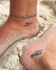 two feet in the sand with blue waves on them and one has a turquoise wave tattoo