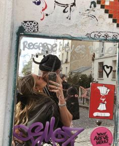 a woman taking a selfie in front of a mirror that has graffiti on it