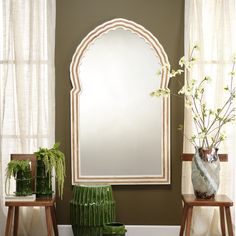 a large mirror sitting on top of a wooden table next to two vases filled with flowers