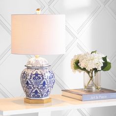 a blue and white vase sitting on top of a table next to a book with a lamp