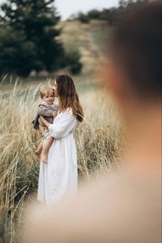 a woman holding a baby in her arms while standing in the middle of a field