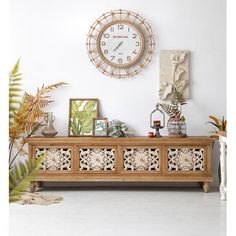 a large clock mounted to the side of a wall above a wooden cabinet filled with plants