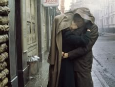 a man and woman kissing on the street in front of a store with an umbrella over their heads