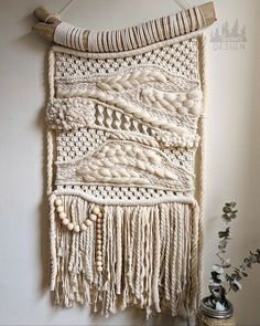 a wall hanging made out of macrame yarn and wood bead, next to a potted plant