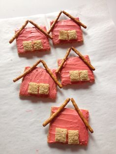 four cookies shaped like houses with sticks sticking out of the top and one has a cracker in the middle