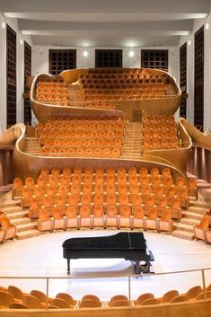 an empty auditorium filled with orange chairs and a black piano in the middle of the room