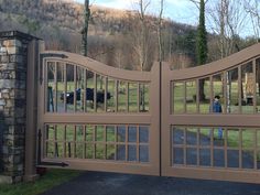 a gated driveway leading to a grassy field with cows in the distance and trees behind it