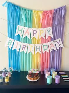 a birthday party with rainbow streamers, cake and cupcakes on the table