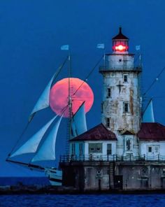 a sailboat sailing past a lighthouse with the moon in the background