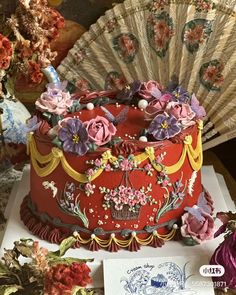 an elaborately decorated red cake sits on a table next to flowers and a fan