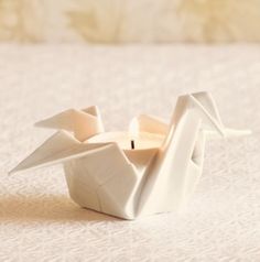 a white candle holder with an origami bird on it's side sitting on a bed