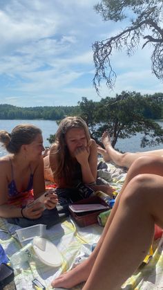 two women sitting on a blanket near the water