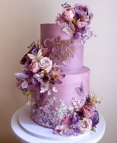 a three tiered purple cake with flowers on it's side and the words happy birthday written on top