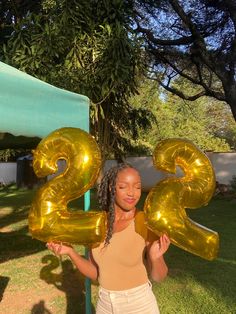 a woman holding up two gold balloons in the shape of numbers