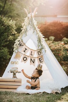 a baby sitting in front of a teepee with the words wild one on it